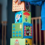 A child playing indoors, stacking colorful wooden toy blocks with joyful illustrations.