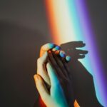 Artistic representation of unity with hands holding under colorful rainbow light reflection.